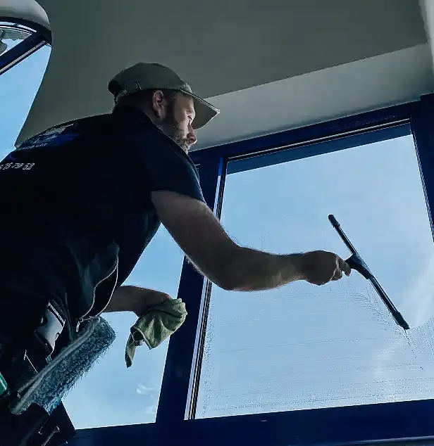 Technicien JP Wash nettoyant une grande baie vitrée à l’aide d’une raclette lors d’un service de nettoyage professionnel de bâtiment.