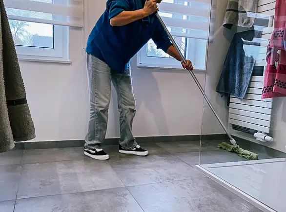 Technicienne JP Wash nettoyant le sol d’une salle de douche lors d’une intervention de nettoyage à domicile