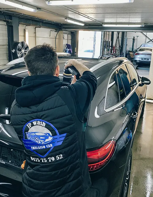 Technicien JP Wash en train de polir la carrosserie d’un véhicule en atelier avec une polisseuse professionnelle, finition esthétique haut de gamme.